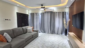 A modern living room with a grey sofa, patterned curtains, a ceiling fan, and a mounted TV.