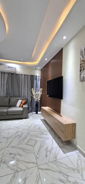 A modern living room with a sofa, TV, and wooden bench. - beautifully updated, centrally located offering air-conditioning in every room (Greater Accra Region)