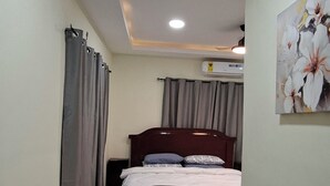 A bedroom with a bed, curtains, a ceiling light, and a wall-mounted air conditioner.