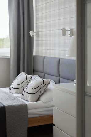 Ein Schlafzimmer mit Bett, Nachttisch, Lampe und einem Fenster mit Vorhängen.