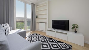 Un soggiorno moderno con un divano, una TV su un mobile bianco, un tappeto decorato e un balcone con tende.