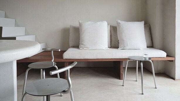 Une pièce au décor minimaliste, comprenant un canapé, deux fauteuils, une petite table et un escalier.