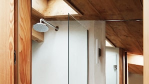 Une douche équipée d’un pommeau de douche à main, un cadre de porte en bois et un mur en béton.