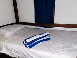 Una cama individual con ropa de cama blanca y toallas azules, un cabecero de madera y una cortina azul oscuro.