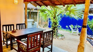 Eine Terrasse im Freien mit einem Holztisch und -stühlen, einem Reetdach und einer blauen Wand mit Wandmalerei.