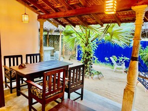 Un patio al aire libre con una mesa y sillas de madera, techo de paja y pared azul con un mural.
