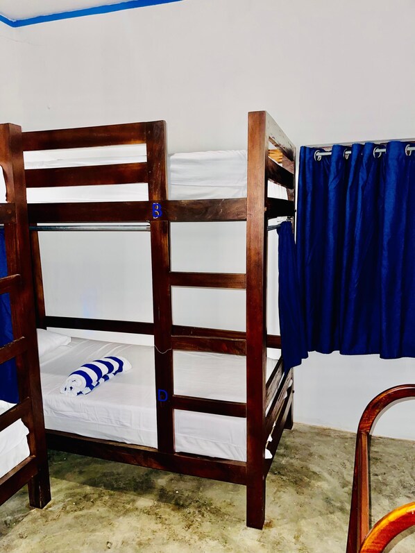 Una cama litera con un almohadón azul a rayas, una cortina azul y una silla de madera.