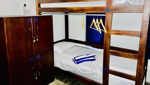 Ein Etagenbett mit Holzrahmen, ein Kleiderschrank mit mehreren Fächern und ein Fenster mit blauen Vorhängen.