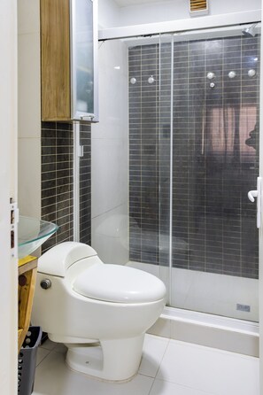 A bathroom with a toilet, a glass shower enclosure, and a tiled wall. - Porlamar Work & Stay Apartment with pool and WIFI (Porlamar)