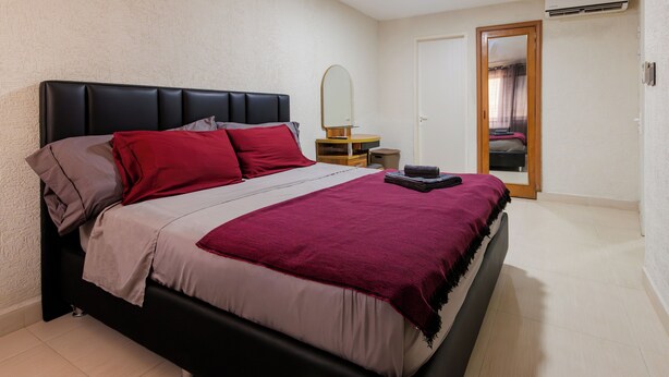 A bedroom with a bed, a bedside table, a mirror, and a door.