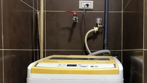A compact, white and yellow water heater in a corner with a wall-mounted control panel and a visible plumbing connection.