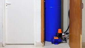 A room with a white door, a blue barrel, and a small heater.