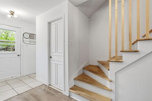 Ein modernes Interieur mit einer weißen Tür, einer Holztreppe und Blick auf Grünfläche.