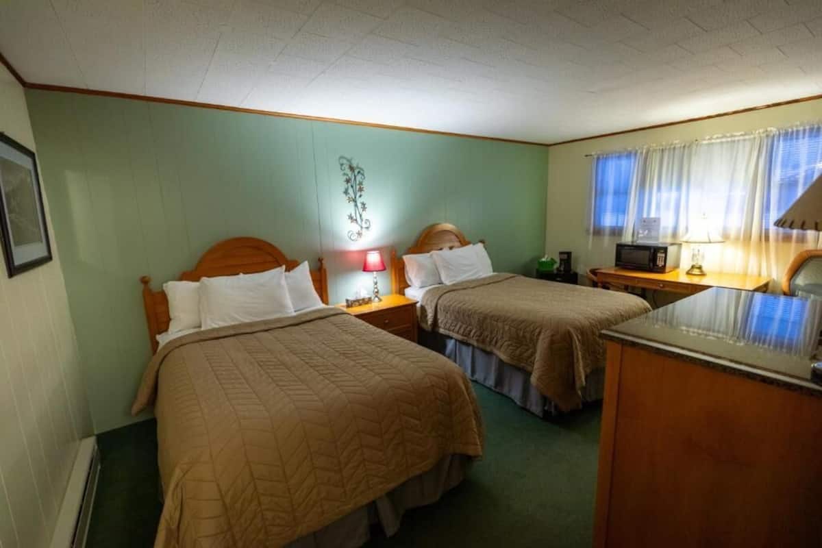 Habitación de hotel con dos camas, un escritorio, un microondas y una mesita de noche con lámpara.
