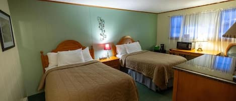 A hotel room with two beds, a desk, a microwave, and a nightstand with a lamp.