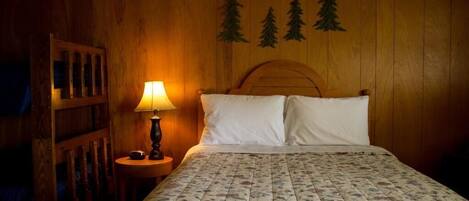 A wooden room with a bed, a nightstand with a lamp, and a wall with tree decorations.
