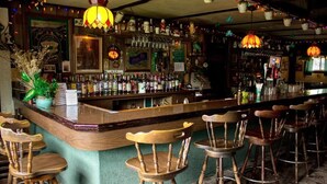 A bar with wooden chairs, a bar counter, and various bottles and glasses. - Jimmy OConnors Windham Mountain Inn (Windham)