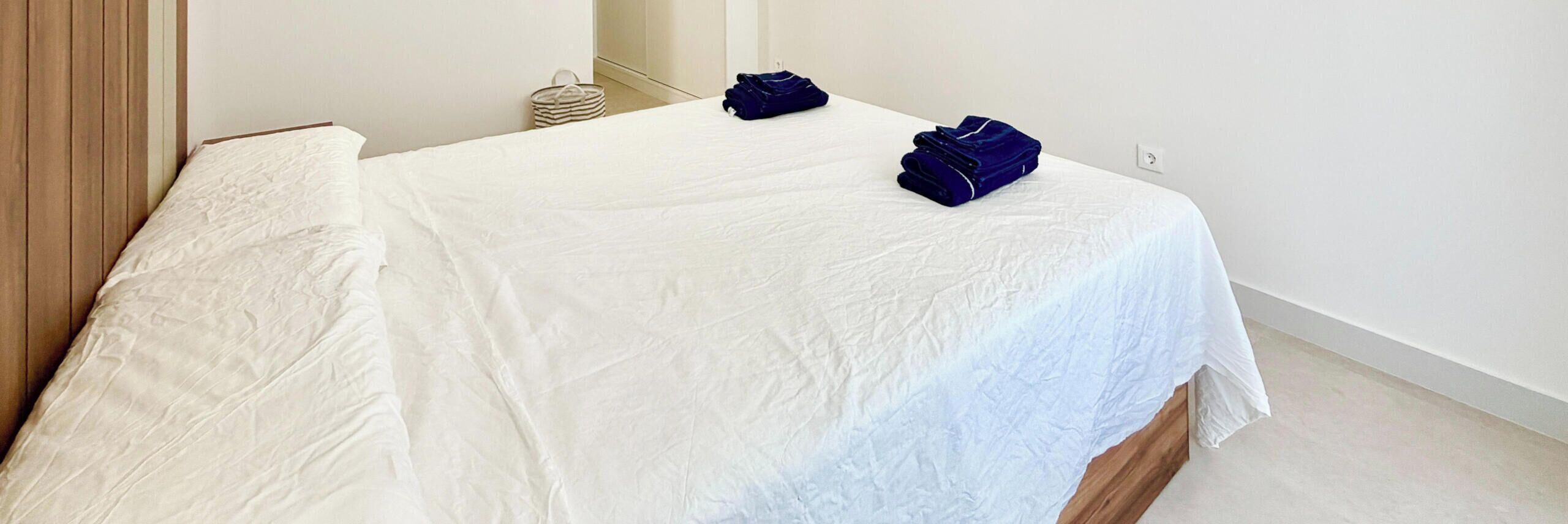 A bed with white linens, a wooden headboard, and a small basket on the floor.
