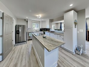 A modern kitchen with white cabinets, a stainless steel refrigerator, a marble countertop, and a built-in oven. - Cindy's Selah (Sneads Ferry)