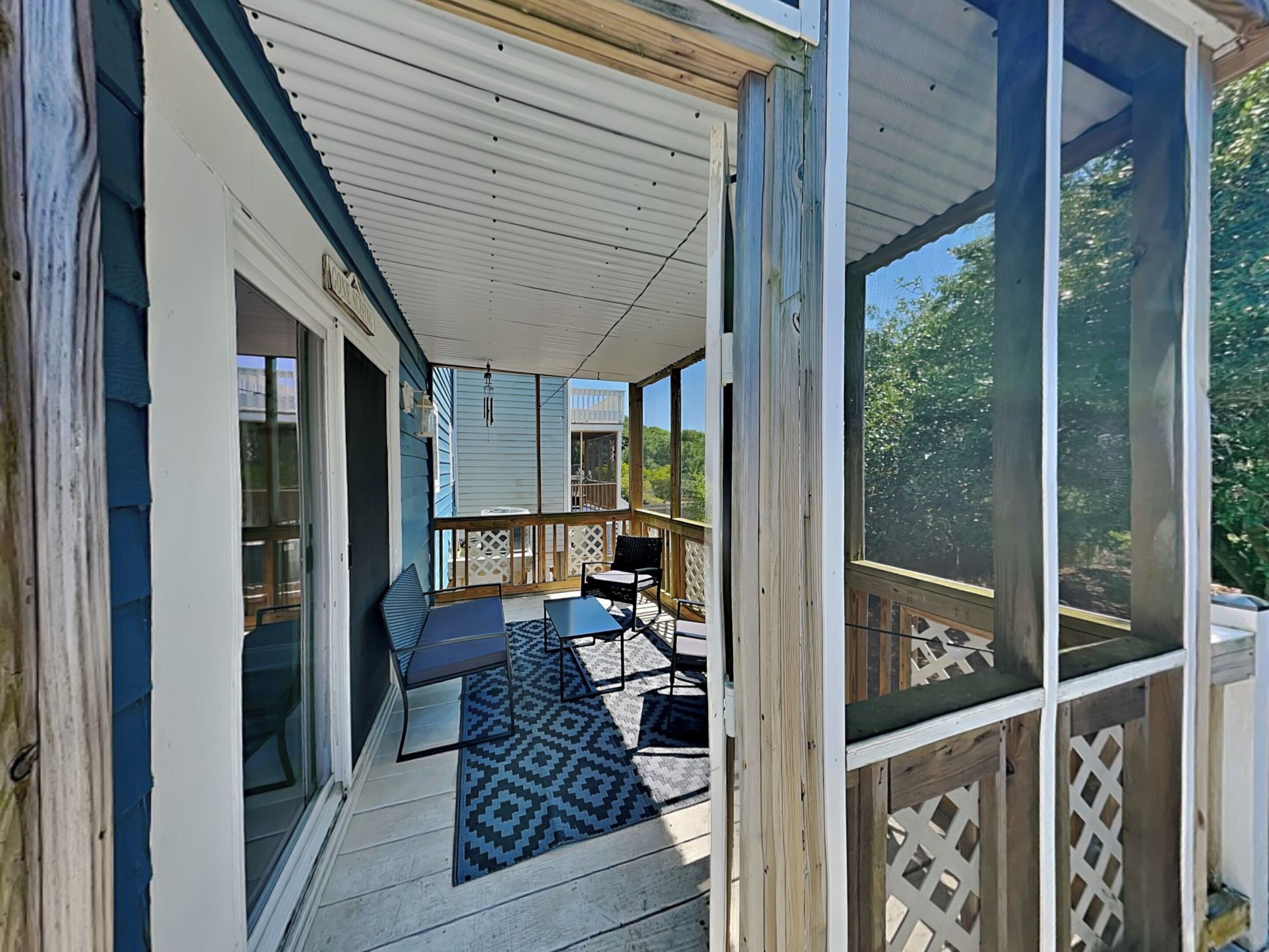 A covered porch with a view of the backyard, a table, chairs, and a patterned rug.