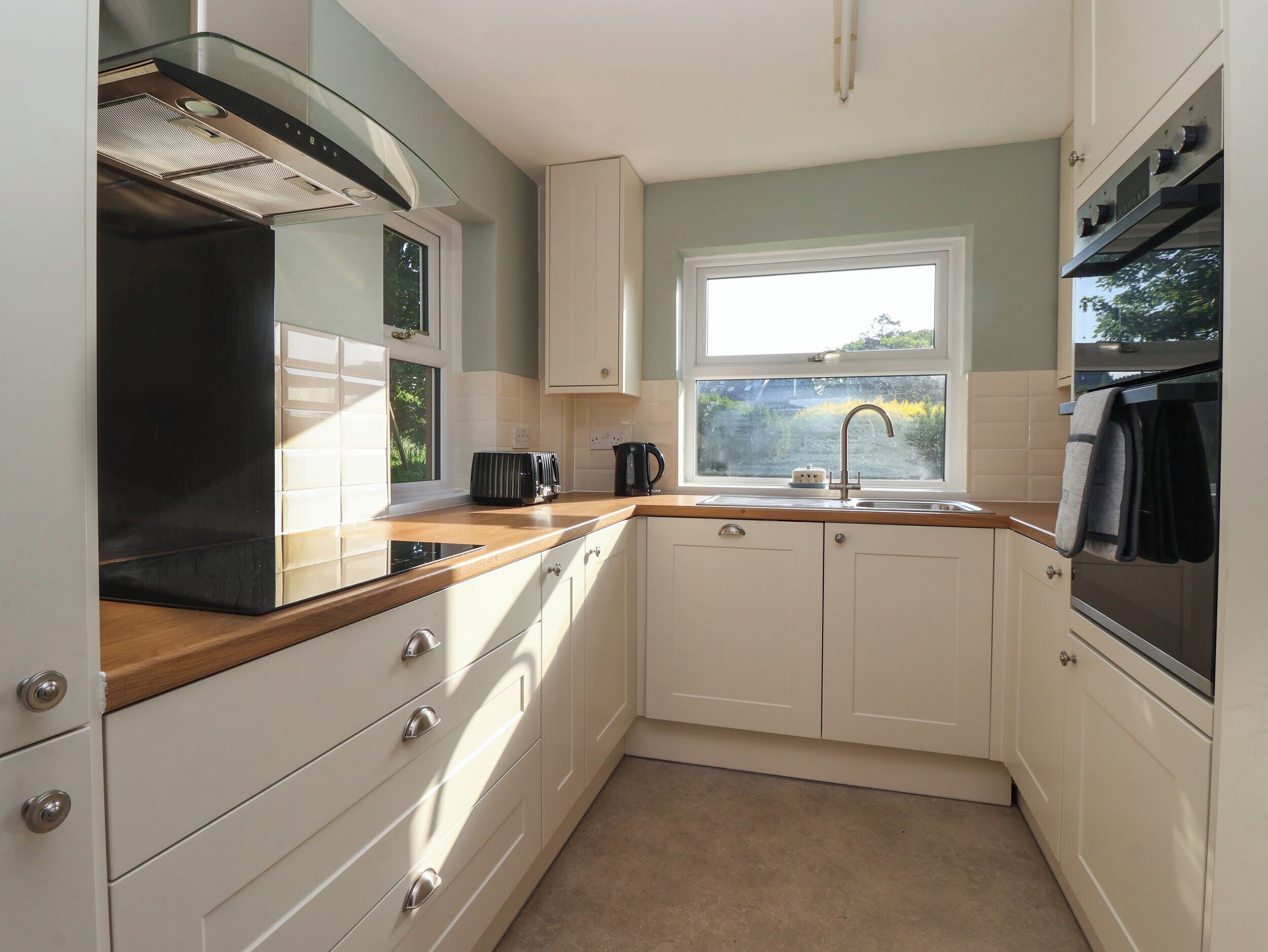 A compact kitchen with white cabinets, a wooden countertop, a window with a view, and a built-in oven.