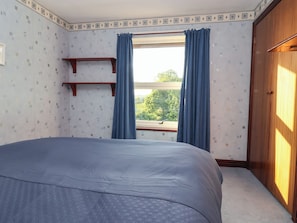 A bedroom with a bed, a window with curtains, a wooden wardrobe, and a shelf. - Robin Hood Farmhouse (Keswick)