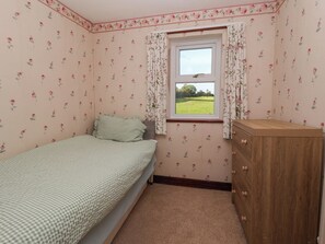 Un dormitorio con una cama individual, un aparador de madera, una ventana con cortinas florales y un estampado de flores en la pared.
