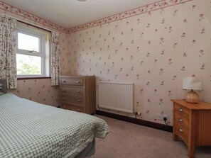 A bedroom with a bed, dresser, radiator, and a window with curtains. - Robin Hood Farmhouse (Keswick)