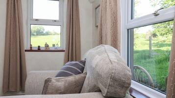 A cozy room with a sofa, a window with curtains, and a view of a green landscape.