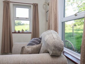 A cozy room with a sofa, a window with curtains, and a view of a green landscape. - Robin Hood Farmhouse (Keswick)