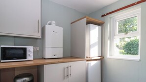 Ett kompakt kök med mikrovågsugn, kylskåp och ett fönster med utsikt över grönområden.