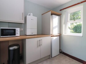 A compact kitchen with a microwave, a refrigerator, and a window with a view of greenery. - Robin Hood Farmhouse (Keswick)