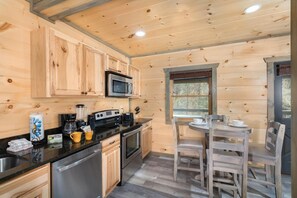 A wooden cabin interior with a kitchen, dining area, and a window.