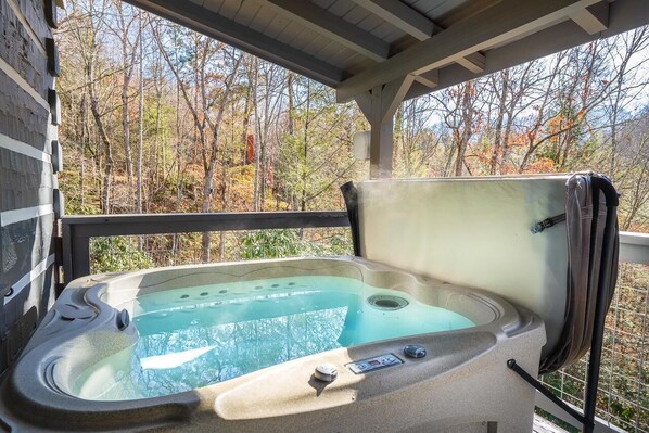 A hot tub with a control panel, a safety rail, and a view of trees.