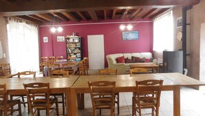Un comedor con mesas y sillas de madera, una estantería, un sofá y una puerta.