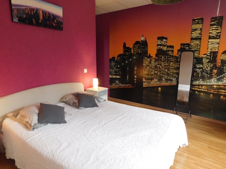 A hotel room with a bed, pillows, a nightstand, a wall-mounted picture, and a cityscape mural.. La maison du parc: the calm of the countryside