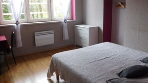 Un dormitorio con cama, mesita de noche, lámpara colgante, ventana con cortinas y un radiador.