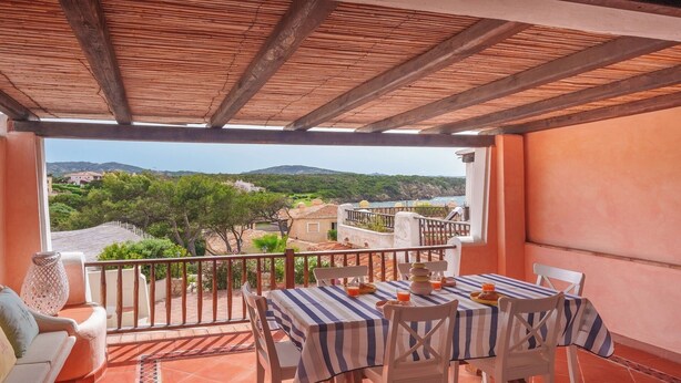 A balcony with a table set for two, overlooking a scenic view of a coastal landscape. - NG Collection Cala del Faro 206 (Arzachena)