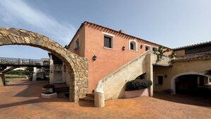 A building with a stone archway, a staircase, and a paved courtyard. - NG Collection Cala del Faro 206 (Arzachena)