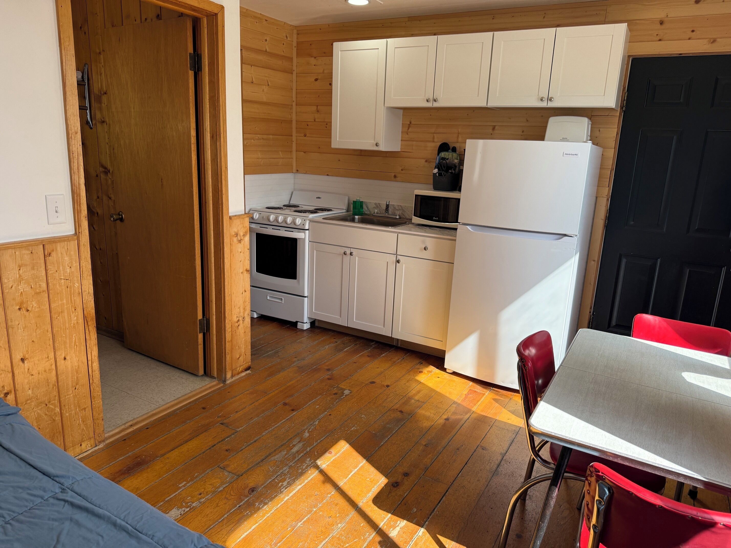 A compact kitchen with wooden flooring, white cabinets, a stove, a microwave, and a refrigerator.