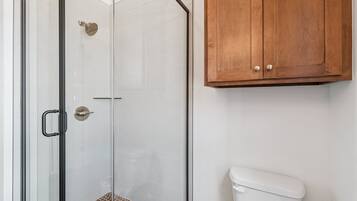 Une salle de bain avec une douche à parois de verre, des toilettes blanches et des meubles en bois.