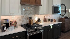 A kitchen with white cabinets, a marble backsplash, a gas stove, and a microwave.