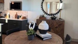 A modern kitchen with white cabinets, a microwave, a round mirror with a black frame, and a dining table with chairs.
