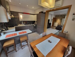 A modern kitchen with a dining area, featuring a wooden dining table, a kitchen island, and a built-in oven. - Andrew's House (Napoli)