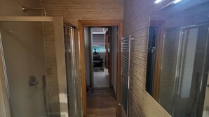 Moderni kylpyhuone, jossa on lasinen suihkuseinä, valkoinen pesuallas ja suuri peili.