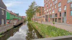 Un canal bordé de bâtiments des deux côtés, un pont en bois et un arbre.