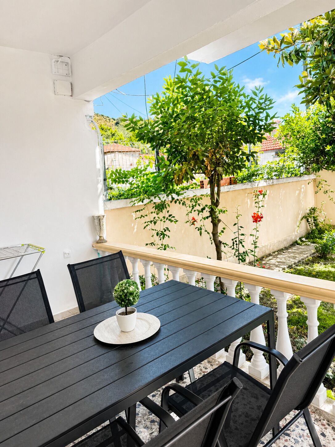 Un patio exterior cubierto con una mesa y sillas, rodeado de vegetación y vistas a una zona residencial.