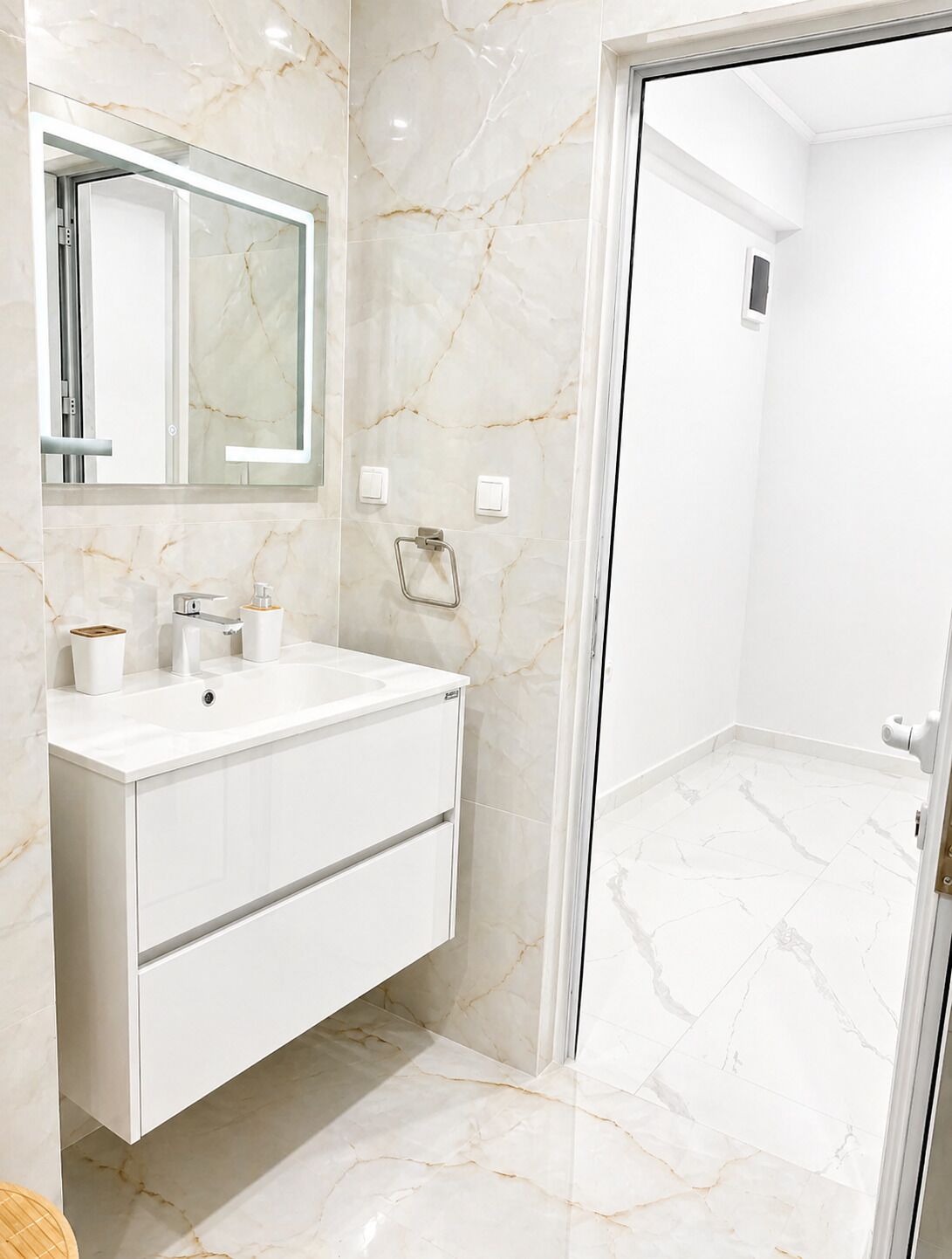 A bathroom with a white vanity, marble walls, a mirror, and a shower area.