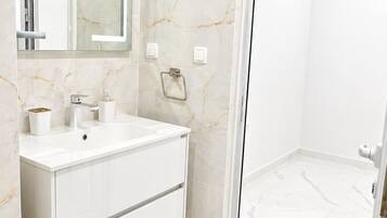A bathroom with a white vanity, marble walls, a mirror, and a shower area.