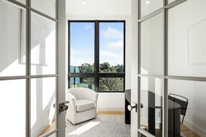 A room with a large window, a white chair, a black table, and a glass partition. - Downtown Traverse City Penthouse w/ Private Rooftop (Traverse City)
